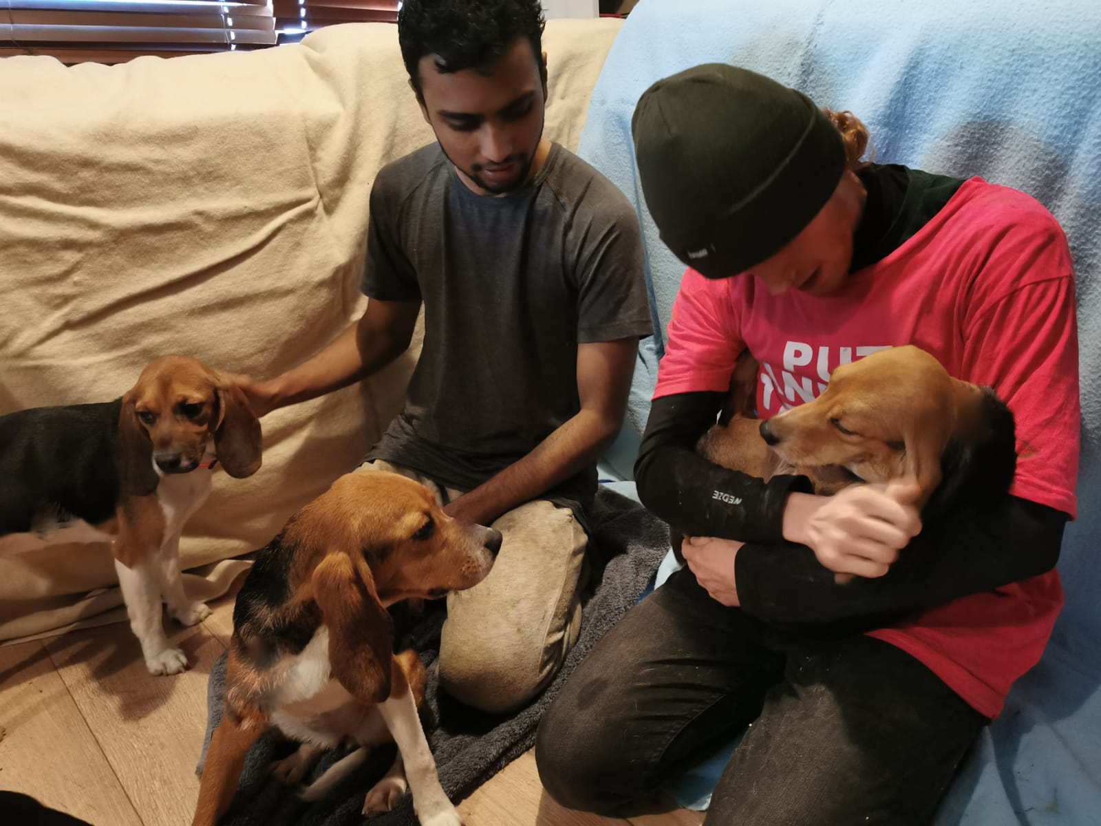 Two men lovingly hold puppies in an undisclosed room, sitting on blankets